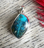 Blue stone pendant on a silver chain with red fabric in the background