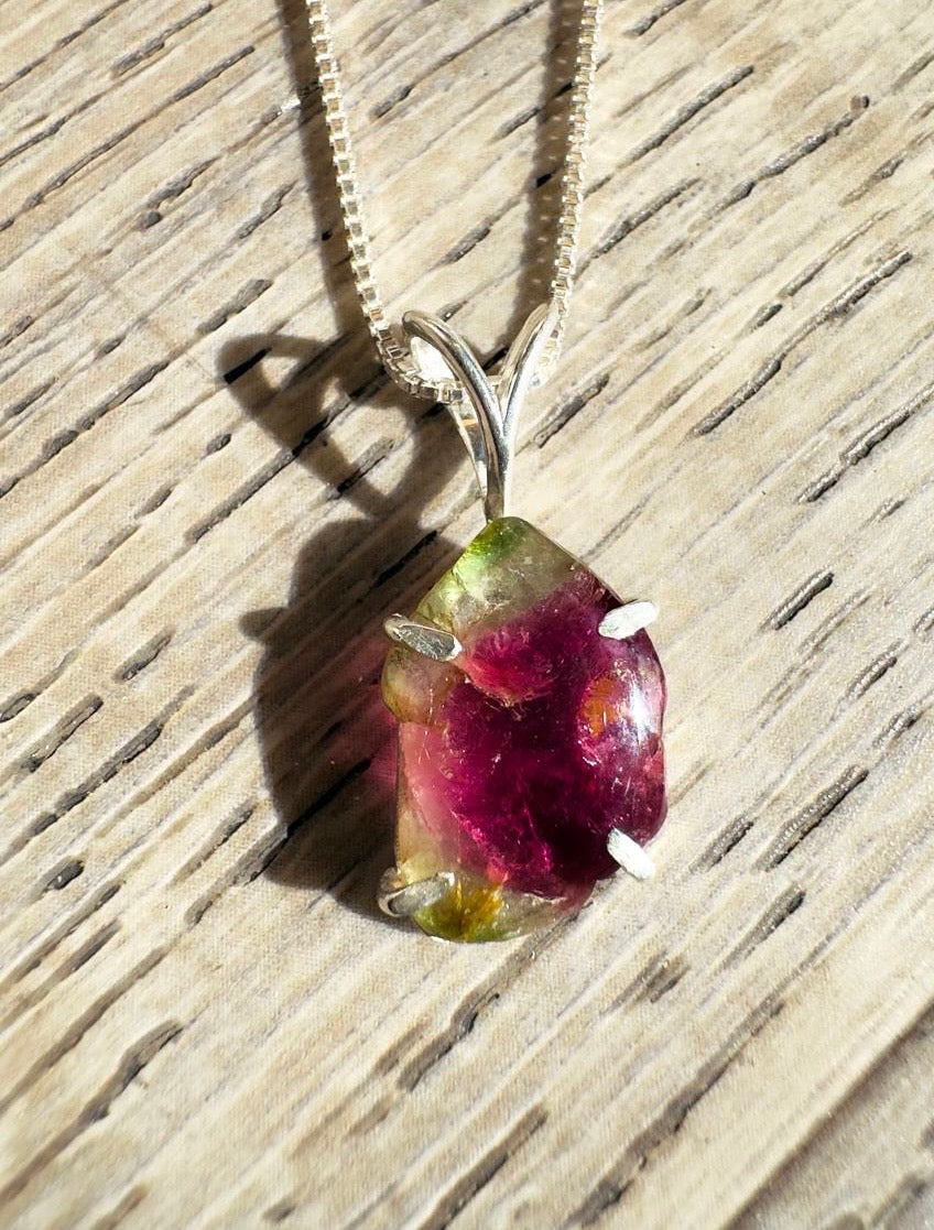 Necklace with a pendant featuring a red and green gemstone on a wooden surface