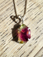 Necklace with a pendant featuring a red and green gemstone on a wooden surface