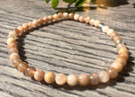 Beaded necklace on a wooden surface with a plant in the background